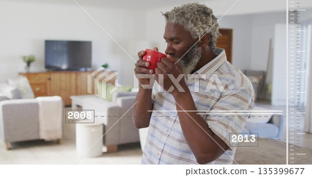 Sipping man in striped shirt raising red mug in living room, with media console, copy space 135399677