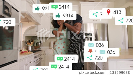 Hugging couple wearing aprons cooking in kitchen, with pots on stove and floating social icons Hugging couple wearing aprons cooking in kitchen, with pots on stove and floating social icons 135399688