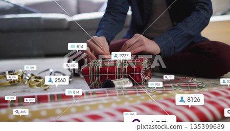 Wrapping woman placing plaid paper on gift at living room floor, with ribbon spool and overlays 135399689