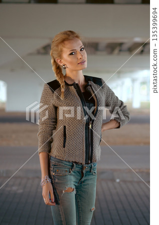 Model poses in urban setting under bridge while wearing denim jeans and a stylish jacket 135399694