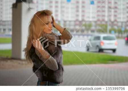 Woman stands under a structure while adjusting her hair in an urban setting during the day Woman stands under a structure while adjusting her hair in an urban setting during the day 135399706