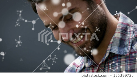Smiling man in plaid shirt, looking downward in grey studio, with molecular graphics, copy space 135399723