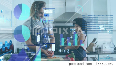 Couple in aprons chopping carrots and consulting smartphone at kitchen island with floating data Couple in aprons chopping carrots and consulting smartphone at kitchen island with floating data 135399769