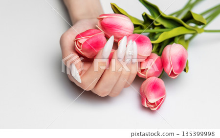 Hand holding pink tulips displaying long white nails 135399998