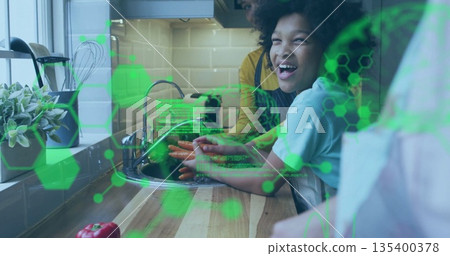 Two women in casual tees washing carrots under faucet in kitchen, with molecular graphics overlay Two women in casual tees washing carrots under faucet in kitchen, with molecular graphics overlay 135400378