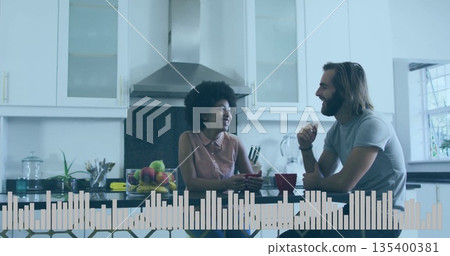 Talking couple holding red mugs and smiling at home kitchen island, with fruit bowl, utensil holder 135400381