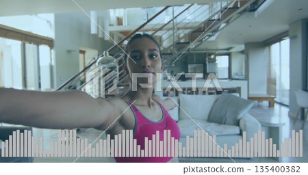 Stretching woman wearing pink sports top extending arms in open plan living room, with white sofa Stretching woman wearing pink sports top extending arms in open plan living room, with white sofa 135400382