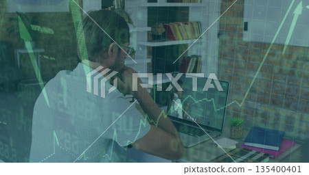 Watching mid adult man at office desk reviewing remote presentation on laptop, with color swatches 135400401