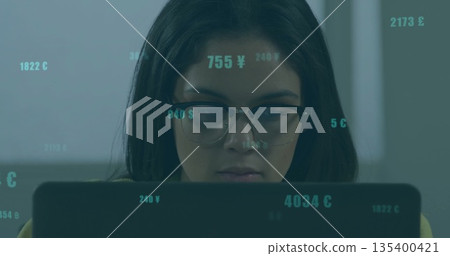 Analyzing finances, Asian woman with eyeglasses using laptop in office, with floating money symbols 135400421