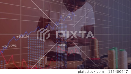 Threading needle tailor wearing T-shirt working on bench in workshop with spools, financial charts Threading needle tailor wearing T-shirt working on bench in workshop with spools, financial charts 135400447