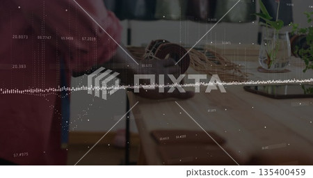 Red shirt man organizing braided cables on wooden workshop table, with smartphone, glass vase plant 135400459