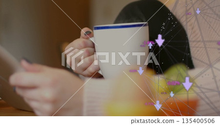 Sipping woman at kitchen table using tablet and holding white mug with blue rim, network overlay Sipping woman at kitchen table using tablet and holding white mug with blue rim, network overlay 135400506
