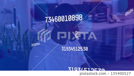 Working African American man analyzing monitor data in modern office, with numeric overlays 135400527
