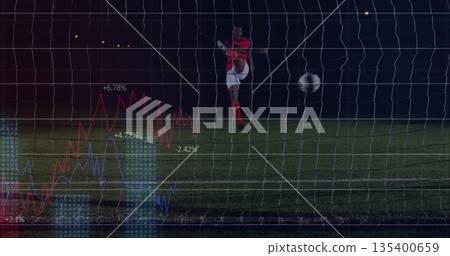 Soccer player kicking ball in red uniform on grass field at night, with net, data overlays 135400659