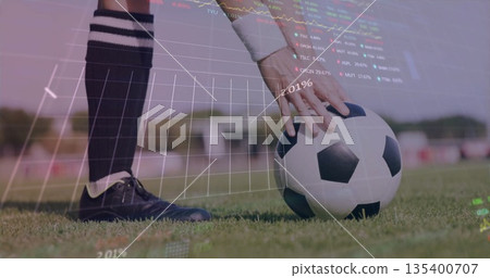 Placing soccer ball on grass pitch by midadult player in cleats, with digital charts overlay 135400707