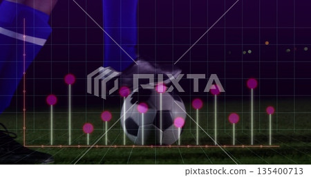Soccer player dribbling soccer ball on turf at night in black cleats, blue socks, data overlay 135400713