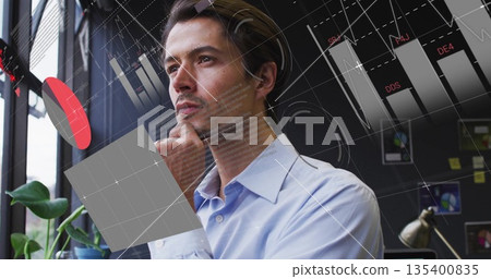 Standing man wearing blue shirt holding chin at office window, with plant and digital graphs Standing man wearing blue shirt holding chin at office window, with plant and digital graphs 135400835