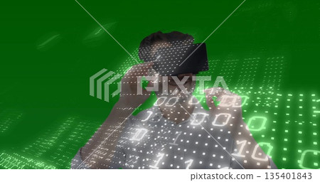 Man in white shirt using VR headset interacting with binary code across green grid in studio 135401843