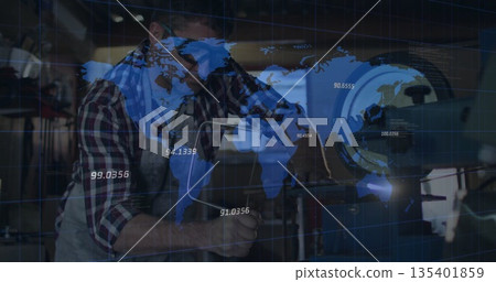 Machinist in apron adjusting cutting tool on lathe at machine shop, with world map overlay Machinist in apron adjusting cutting tool on lathe at machine shop, with world map overlay 135401859