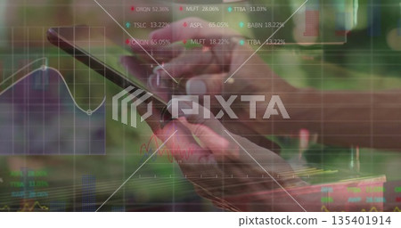 Showing hands holding smartphone at digital workspace, with ticker, line chart and grid overlays 135401914