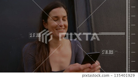Smiling mid adult woman holding smartphone, viewing digital travel dates on dark metal wall Smiling mid adult woman holding smartphone, viewing digital travel dates on dark metal wall 135401929