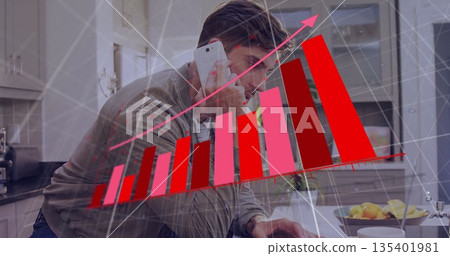 Leaning male analyzing red bar chart on laptop at kitchen island holding phone with grid overlay Leaning male analyzing red bar chart on laptop at kitchen island holding phone with grid overlay 135401981