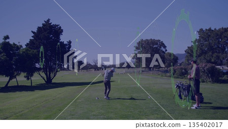 Swinging club by golfer wearing polo shirt hitting ball on tee on fairway, with golf bag 135402017