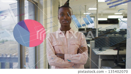 Standing woman wearing pink button up shirt observing data visualizations in office, with analytics 135402070