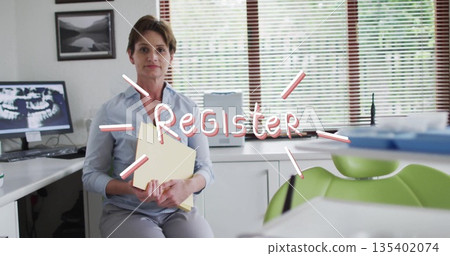 Receptionist in blue shirt organizing yellow patient folders at dental reception, with Xray monitor 135402074