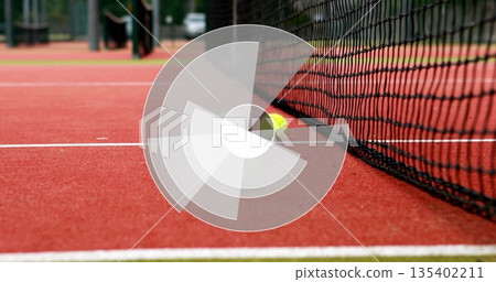 Resting yellow tennis ball leaning against black net on red clay court boundary lines, copy space Resting yellow tennis ball leaning against black net on red clay court boundary lines, copy space 135402211