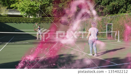Playing mature couple rallying over net on garden tennis court, with rackets and pink smoke Playing mature couple rallying over net on garden tennis court, with rackets and pink smoke 135402212