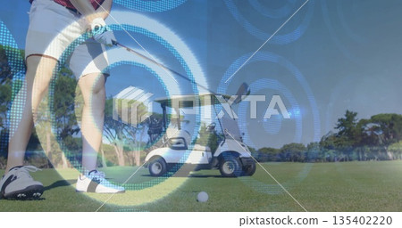 Swinging male golfer gripping club and targeting teed ball on fairway, with golf cart, copy space 135402220