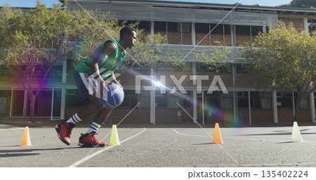 Dribbling man in green top guiding blue basketball around cones on outdoor court, copy space 135402224