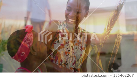 Cleaning window at porch, mother in floral top and daughter in pink shirt laughing with squeegee 135402267