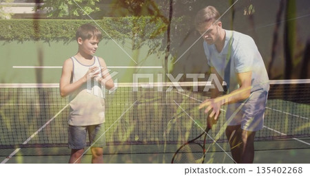 Father and son practicing tennis on backyard court with racket balancing balls on net over lines 135402268