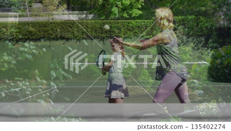 Tossing tennis ball mother in sportswear coaching daughter on home court with racket net plants Tossing tennis ball mother in sportswear coaching daughter on home court with racket net plants 135402274