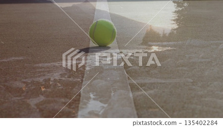 Resting tennis ball sitting on white painted line on outdoor court, with puddles and stones Resting tennis ball sitting on white painted line on outdoor court, with puddles and stones 135402284