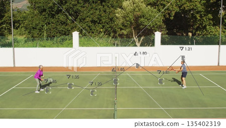 Rallying senior pair in sportswear on outdoor hard court, with rackets net boundary lines fence Rallying senior pair in sportswear on outdoor hard court, with rackets net boundary lines fence 135402319