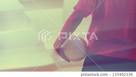 Standing woman in red jersey black shorts holding volleyball at gym under pink lighting, copy space 135402336