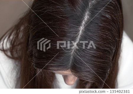 Close up photo brunette woman with gray hair. Female head top view. Gray hair on the parting. Cropped photo close up 135402381