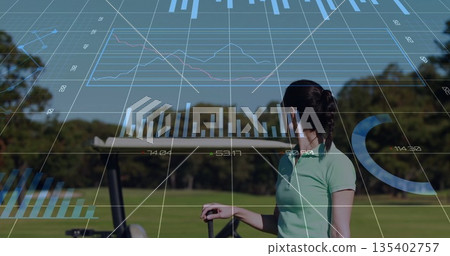Standing female golfer analyzing real-time analytics on golf fairway, with golf club and push cart Standing female golfer analyzing real-time analytics on golf fairway, with golf club and push cart 135402757