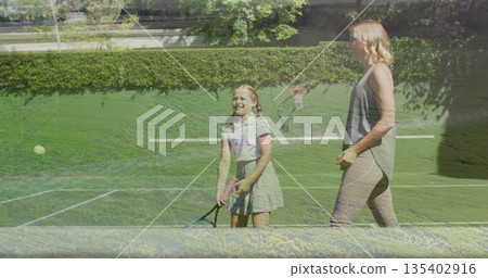 Practicing mother coaching daughter on grass court wearing grey top, skirt, with racket, ball, net 135402916