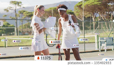 Standing friends in white attire pausing on tennis court, with rackets, bottle, social media icons Standing friends in white attire pausing on tennis court, with rackets, bottle, social media icons 135402933