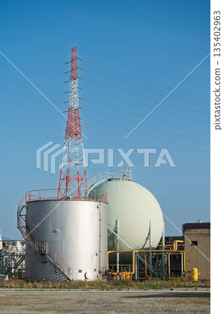 Power transmission towers and industrial tanks at sewage treatment plants - urban infrastructure and energy facilities shining against the blue sky Power transmission towers and industrial tanks at sewage treatment plants - urban infrastructure and energy facilities shining against the blue sky 135402963