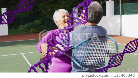 Embracing senior couple wearing sportswear holding rackets at tennis court, with purple DNA helix 135403348