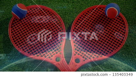 Forming heart shape two red plastic rackets on green turf, with red and blue foam balls 135403349