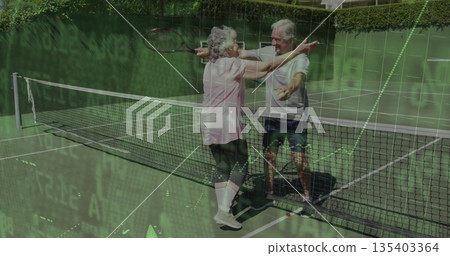 Hugging senior couple in sportswear holding wooden rackets at net on green court, with white lines Hugging senior couple in sportswear holding wooden rackets at net on green court, with white lines 135403364
