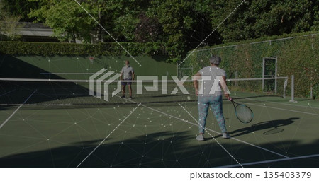 Playing tennis pair standing on private tennis court, holding rackets with balls and metal gate 135403379
