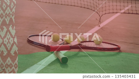 Lying crossed tennis rackets with five yellow balls on outdoor hard court, with net, boundary lines 135403431