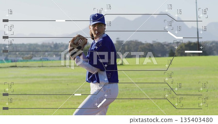 Pitching female player wearing blue uniform and cap on grassy field, with leather glove and ball 135403480